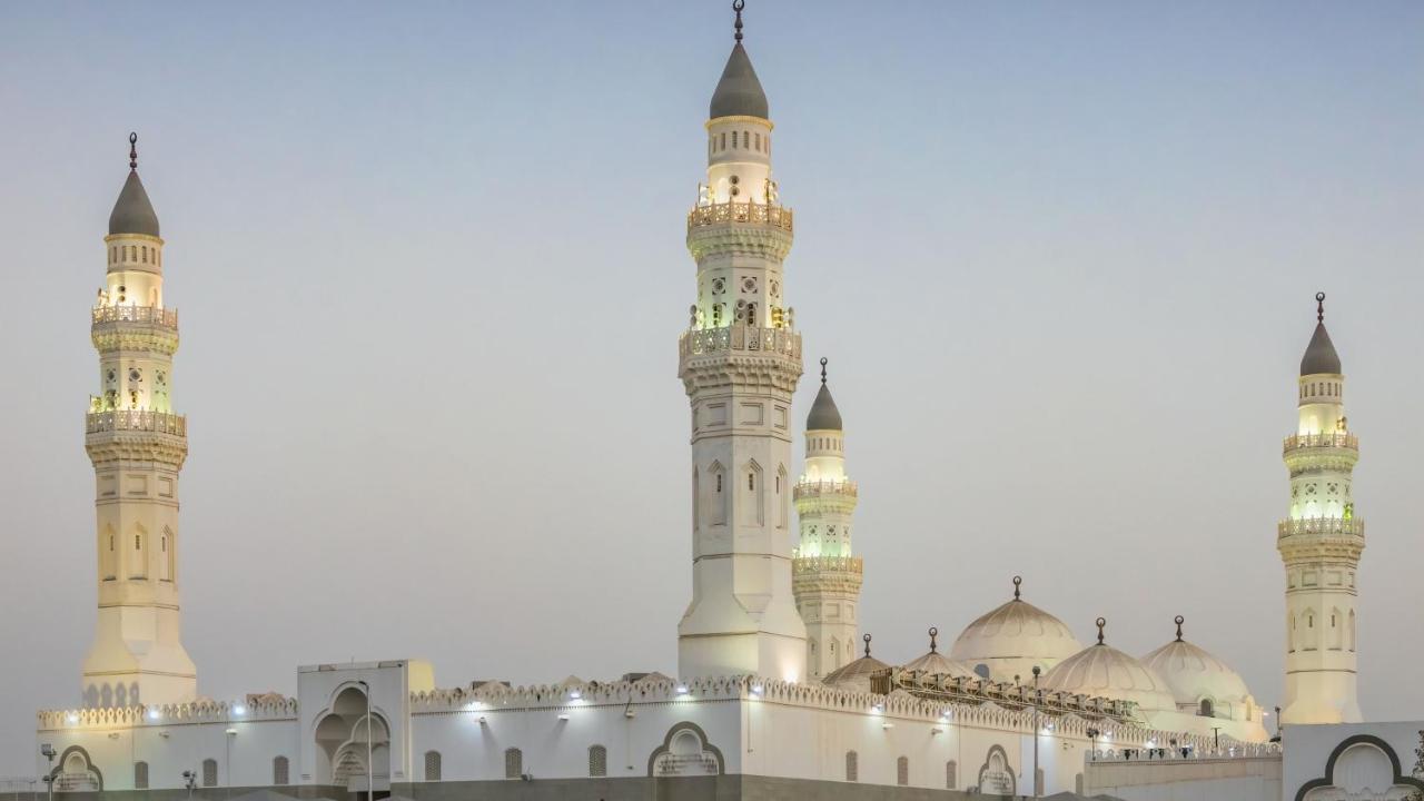 Intercontinental Dar Al Iman Madinah By Ihg Hotel Medina Buitenkant foto The image shows a mosque with distinct architectural features, including tall minarets and domes. The minarets are highlighted, likely lit up in the evening, showcasing intricate design elements typical of Islamic architecture. The overall scene conv