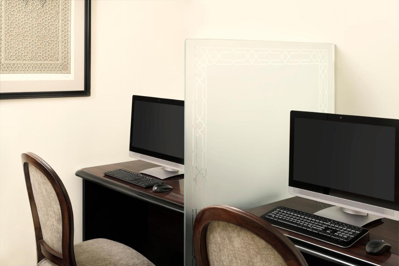 Intercontinental Dar Al Iman Madinah By Ihg Hotel Medina Buitenkant foto The photo shows a workspace featuring two computers set up on a dark wooden desk. Each computer has a monitor and a keyboard. A frosted glass partition is placed between the two workstations, providing some privacy. In the background, there is a fram