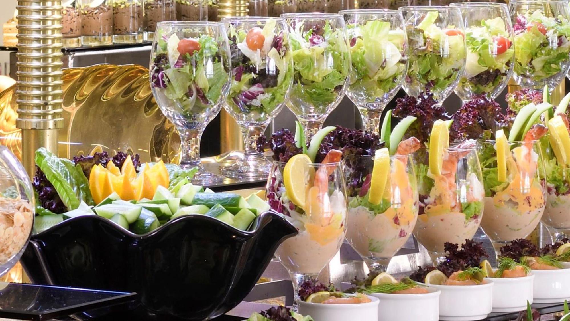 Intercontinental Dar Al Iman Madinah By Ihg Hotel Medina Buitenkant foto The photo features an elegant display of food items. In the background, there are several clear glasses filled with vibrant salads, featuring various types of greens and garnishes. In the foreground, there is a decorative black bowl containing cut pi