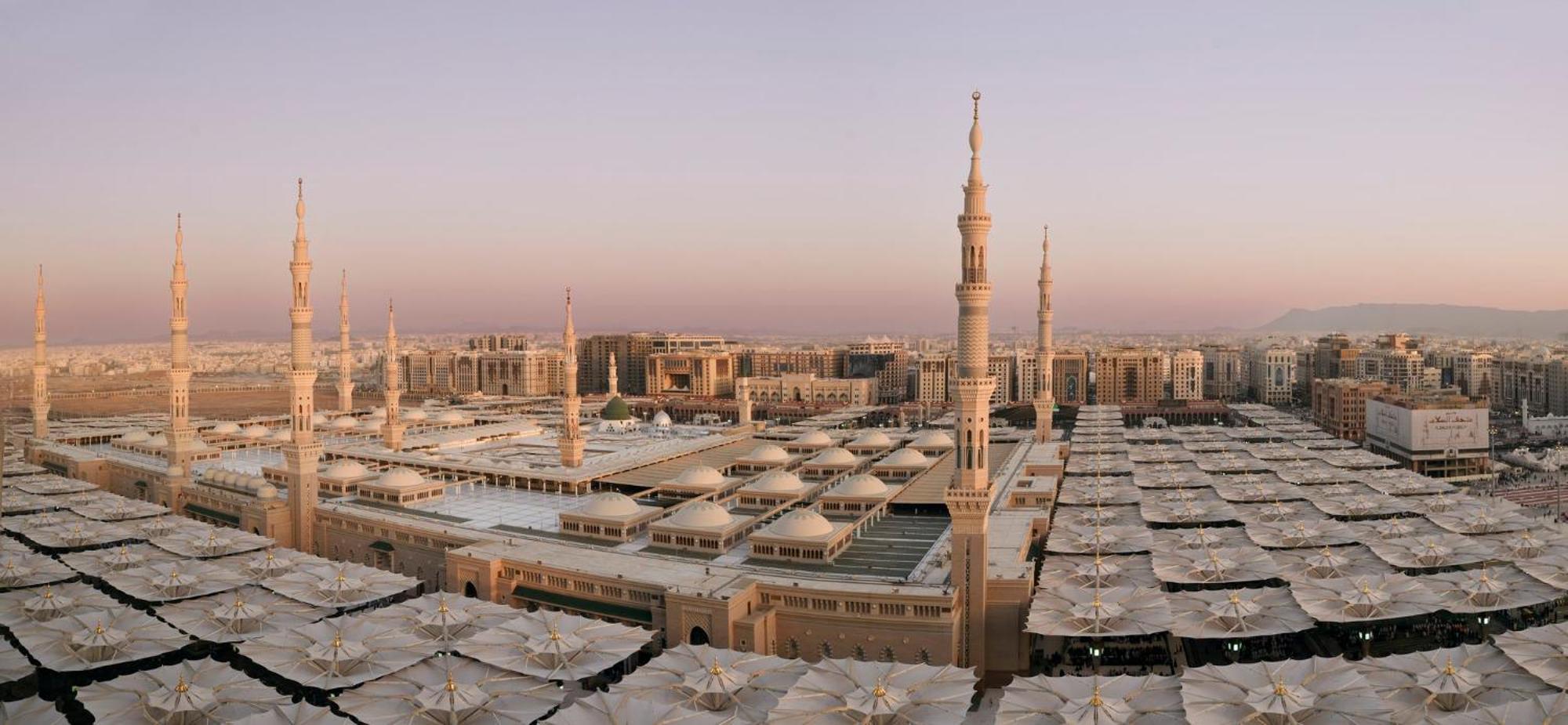 Intercontinental Dar Al Iman Madinah By Ihg Hotel Medina Buitenkant foto The photo shows an aerial view of the Al-Masjid an-Nabawi, or the Prophet's Mosque, located in Medina, Saudi Arabia. The mosque features distinct minarets, large white domes, and expansive open areas with large umbrellas that provide shade for visito