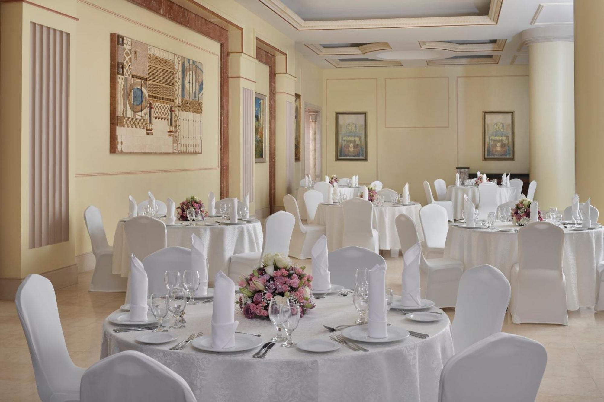 Intercontinental Dar Al Iman Madinah By Ihg Hotel Medina Buitenkant foto The photo shows an elegantly arranged dining or function room. There are round tables covered with white tablecloths, each set with fine dining ware including glassware, utensils, and neatly folded white napkins. Some tables have floral centerpieces 