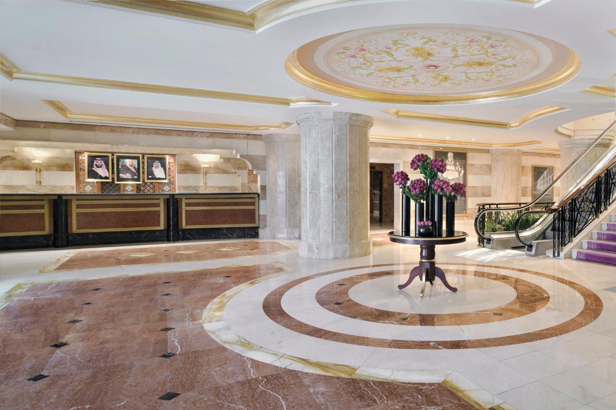 Intercontinental Dar Al Iman Madinah By Ihg Hotel Medina Buitenkant foto The photo shows a luxurious hotel lobby. The space features elegant marble flooring with circular designs, complemented by a large, decorative ceiling. In the center, there is a round table adorned with a floral arrangement. Behind the table, a recep