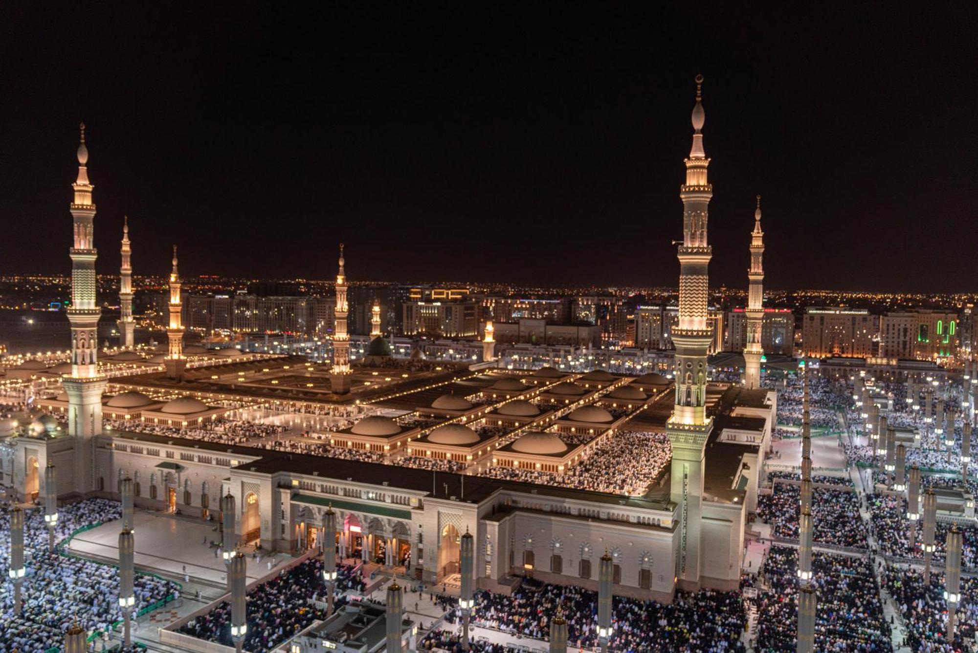 Intercontinental Dar Al Iman Madinah By Ihg Hotel Medina Buitenkant foto The photo shows a panoramic view of a large mosque complex illuminated at night. It features tall minarets with lights, a vast courtyard filled with people, and a beautifully lit architectural design. The overall ambiance suggests a significant space