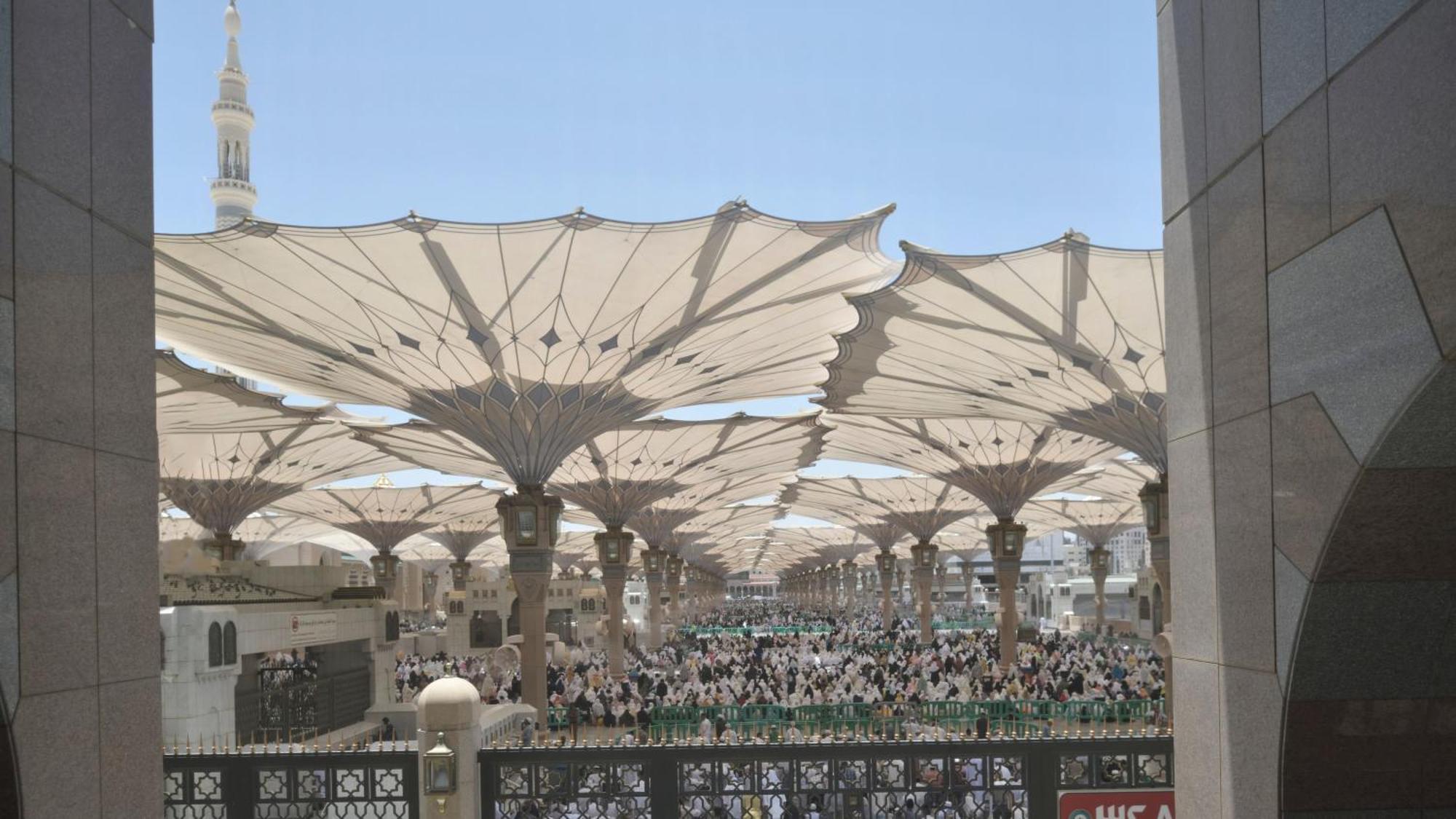 Intercontinental Dar Al Iman Madinah By Ihg Hotel Medina Buitenkant foto The photo shows a large open area covered by expansive canopies, likely designed to provide shade for the people below. Underneath the canopies, there are many individuals gathered, possibly participating in a religious event or gathering. In the bac