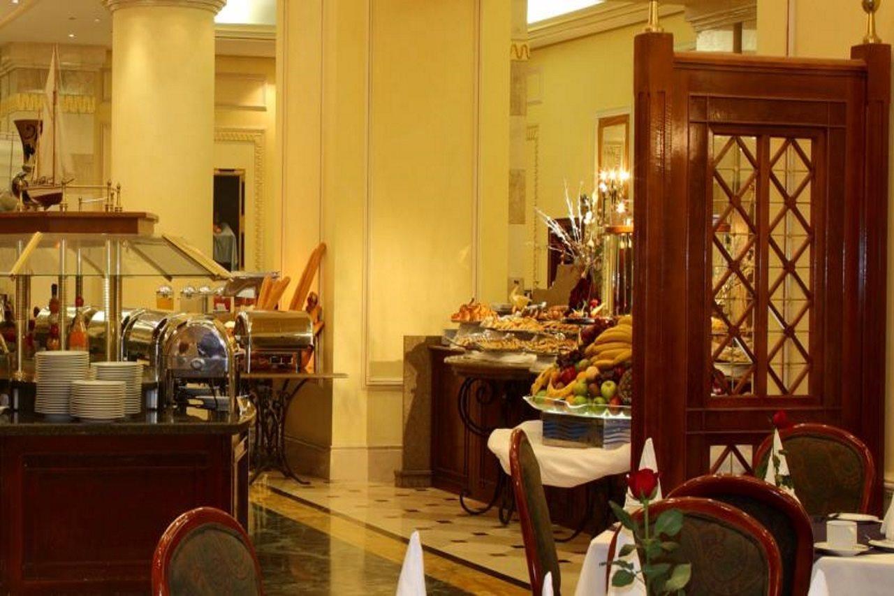 Intercontinental Dar Al Iman Madinah By Ihg Hotel Medina Buitenkant foto The photo shows an elegant dining area, likely within a restaurant or a hotel. There's a buffet setup on one side with various food items displayed, including pastries and fruits. The room features warm lighting, polished floors, and decorative walls