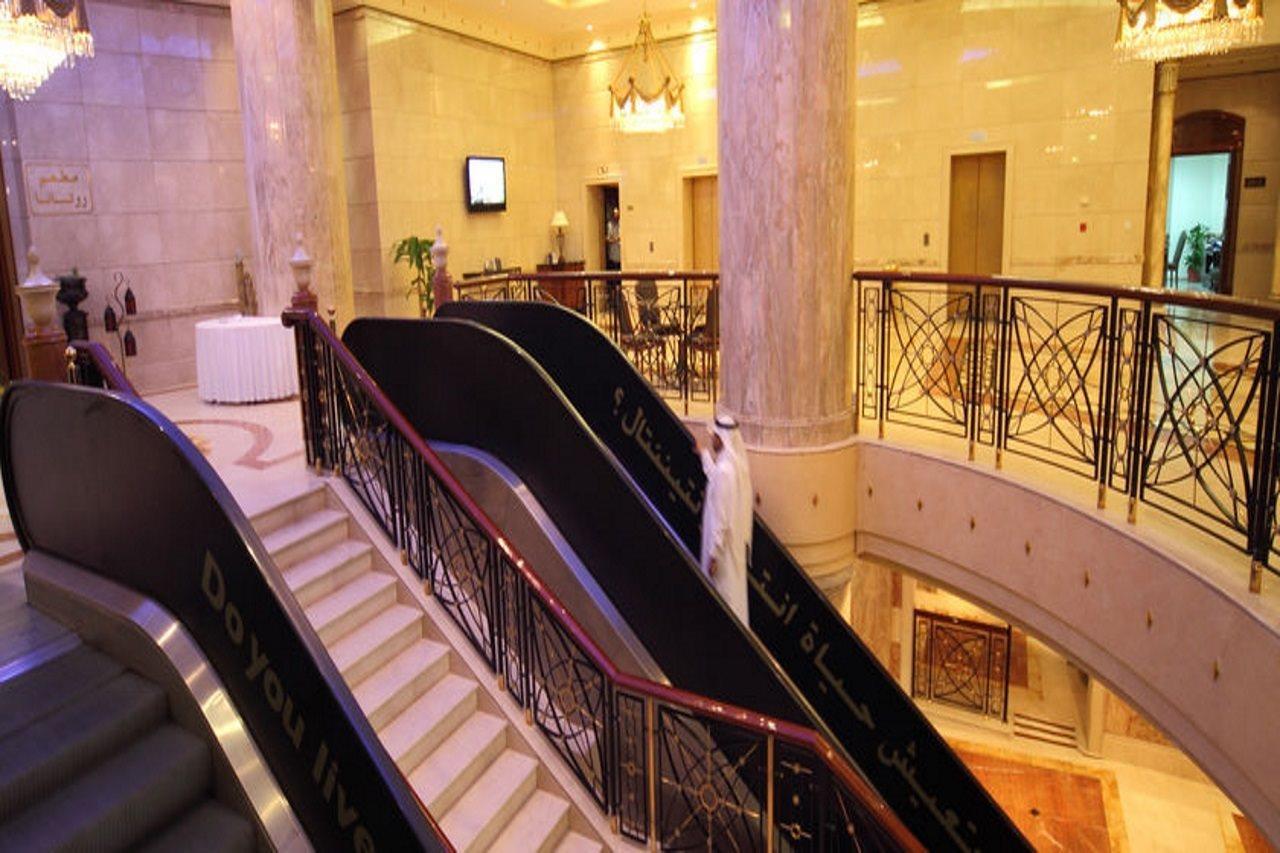 Intercontinental Dar Al Iman Madinah By Ihg Hotel Medina Interieur foto The photo depicts an elegant interior space, likely within a hotel or a large building. There is a grand staircase visible, which features a combination of stairs and escalators. The design includes decorative railings and marble pillars, contributin